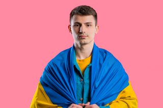 Ein junger Mann schaut in die Kamera, er trägt eine ukrainische Landesflagge um die Schultern gelegt